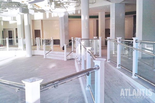 Glass railing panels on indoor ramp staircase chrome and white wood.